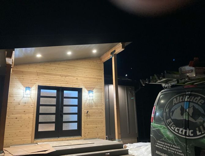 Exterior of a building with illuminated entry lights and a black door. A van with 