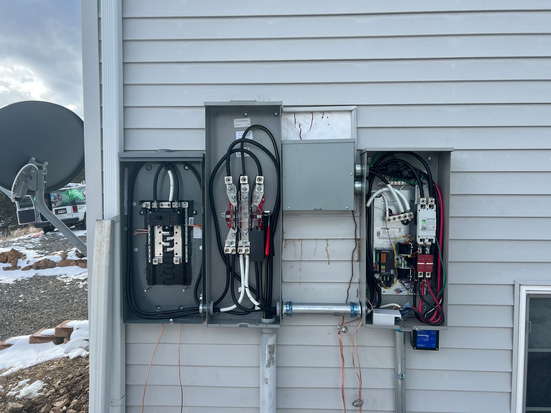 Open electrical panel with black, white, and red wires, circuit breakers, and other components, mounted on a wall.