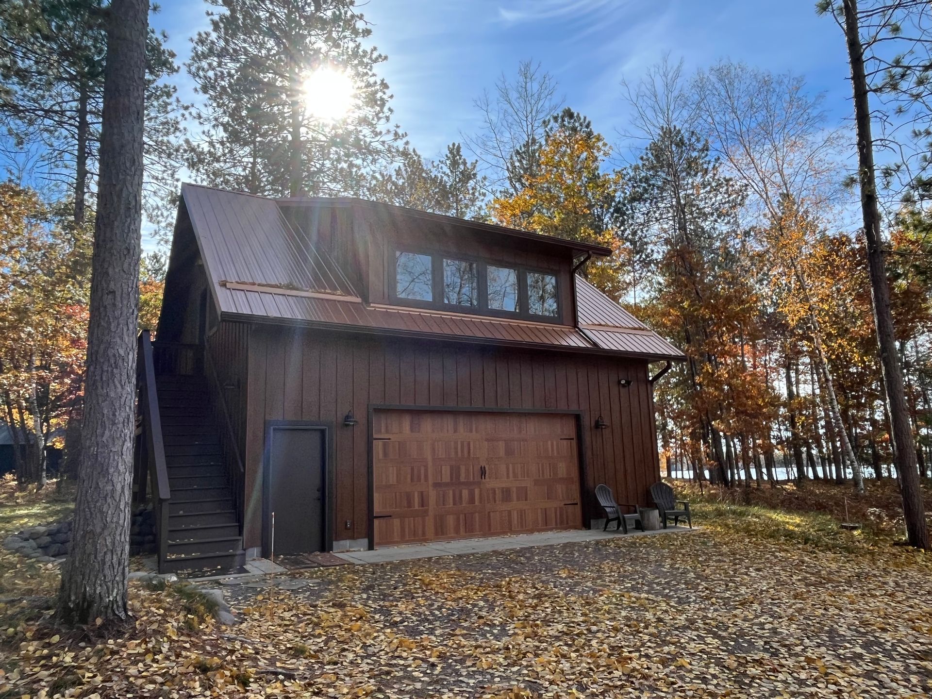 A large wooden garage with stairs leading up to it is surrounded by trees and leaves.