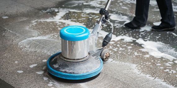 A person is cleaning a concrete floor with a machine.