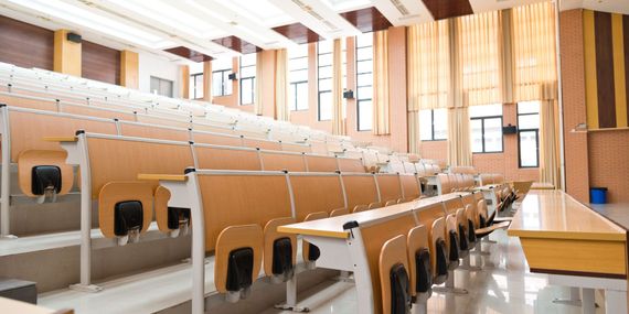 An empty lecture hall with rows of desks and chairs.