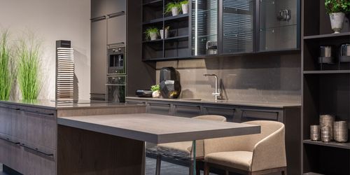 A kitchen with a large island , chairs , a sink and a refrigerator.