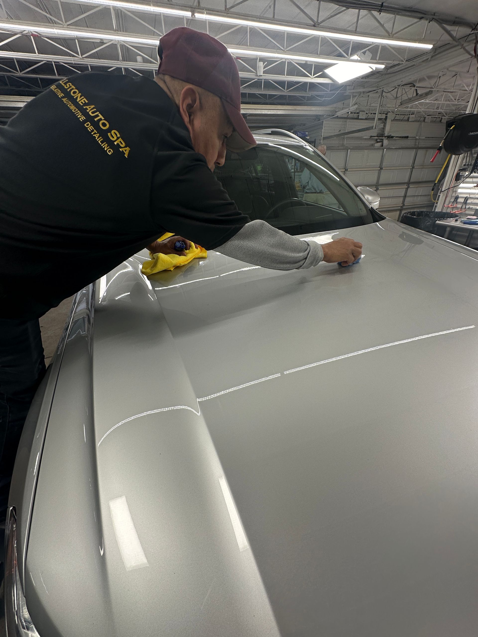 A man is cleaning the hood of a car in a garage.