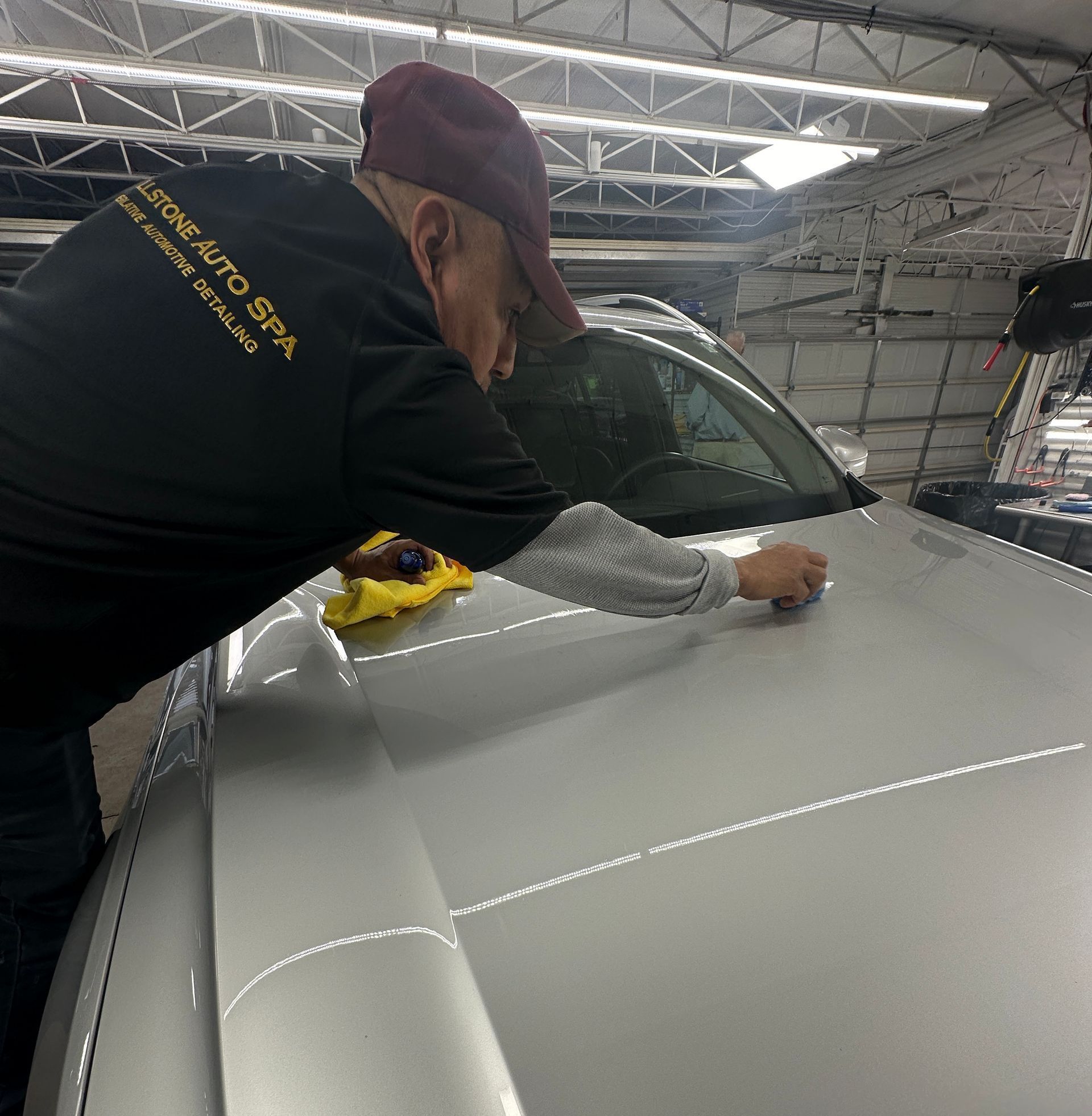 A person wearing black gloves is polishing a car with a sponge.