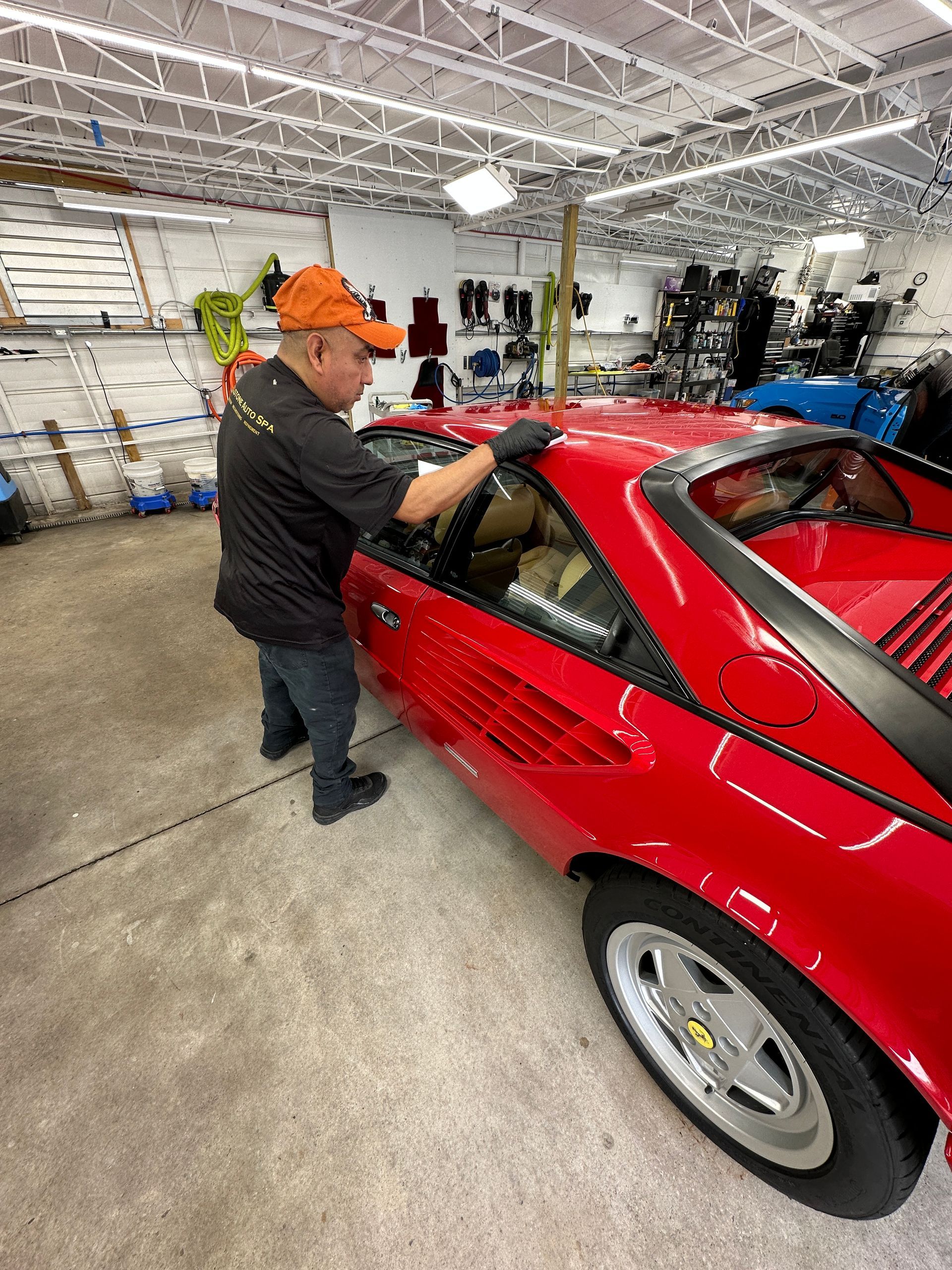 A man is standing next to a red sports car in a garage.