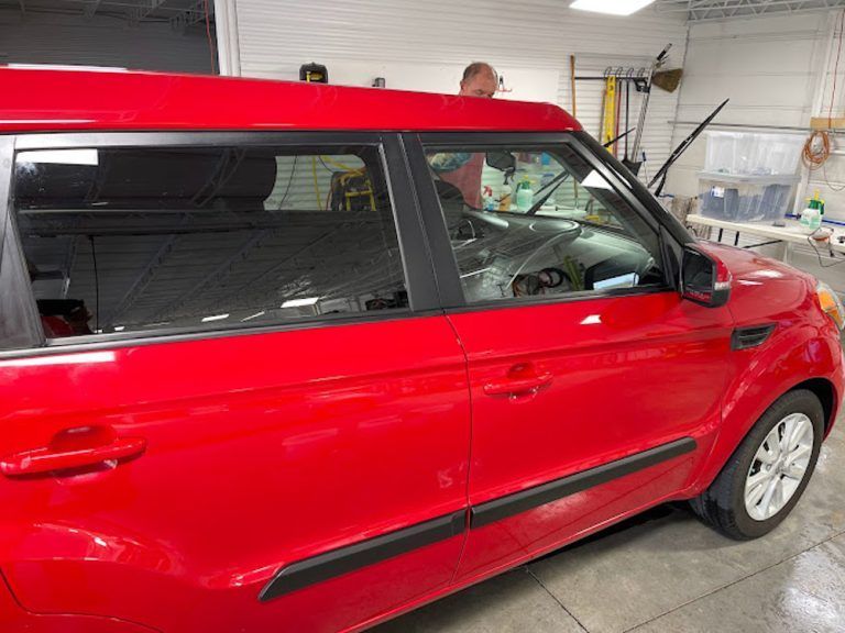 A red car is parked in a garage with a man standing next to it.