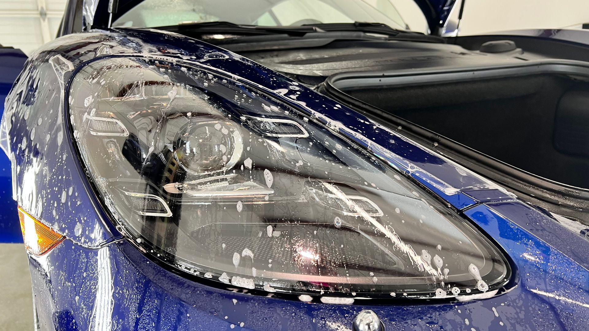 Blue sports car headlight covered in soapy water.