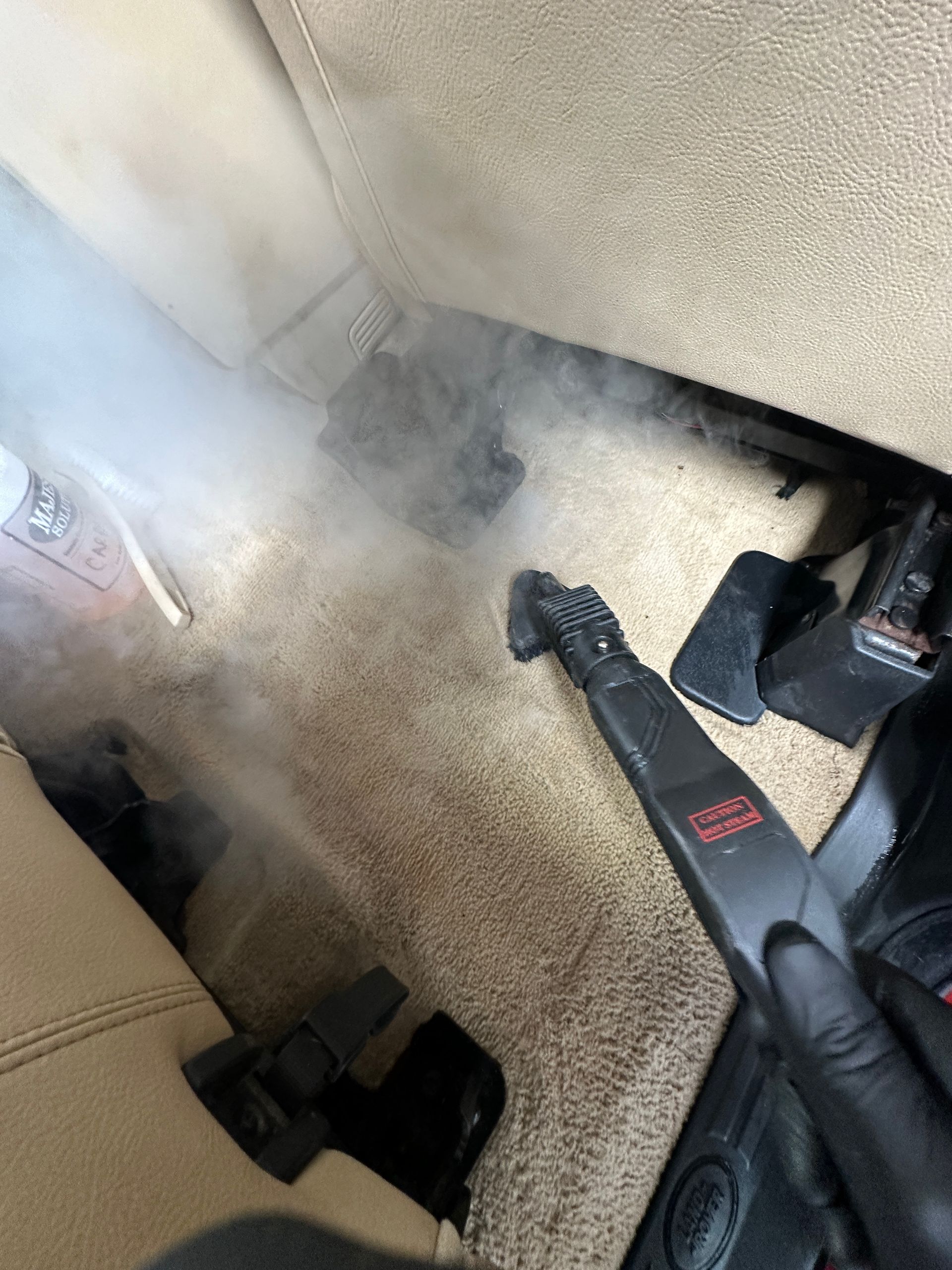 A person is using a steam cleaner to clean the floor of a car.