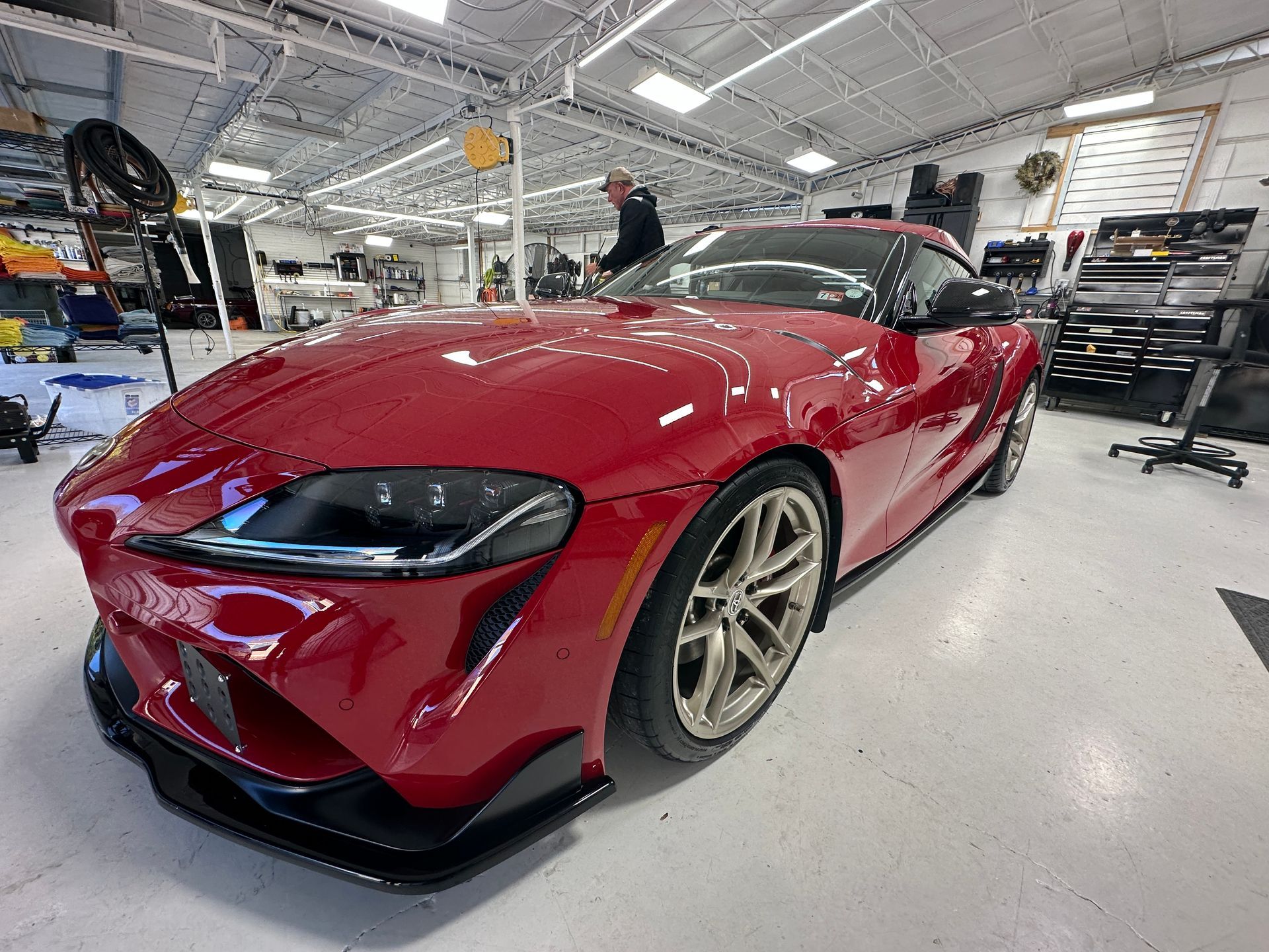 Red Toyota Supra sports car in a garage with a person nearby.