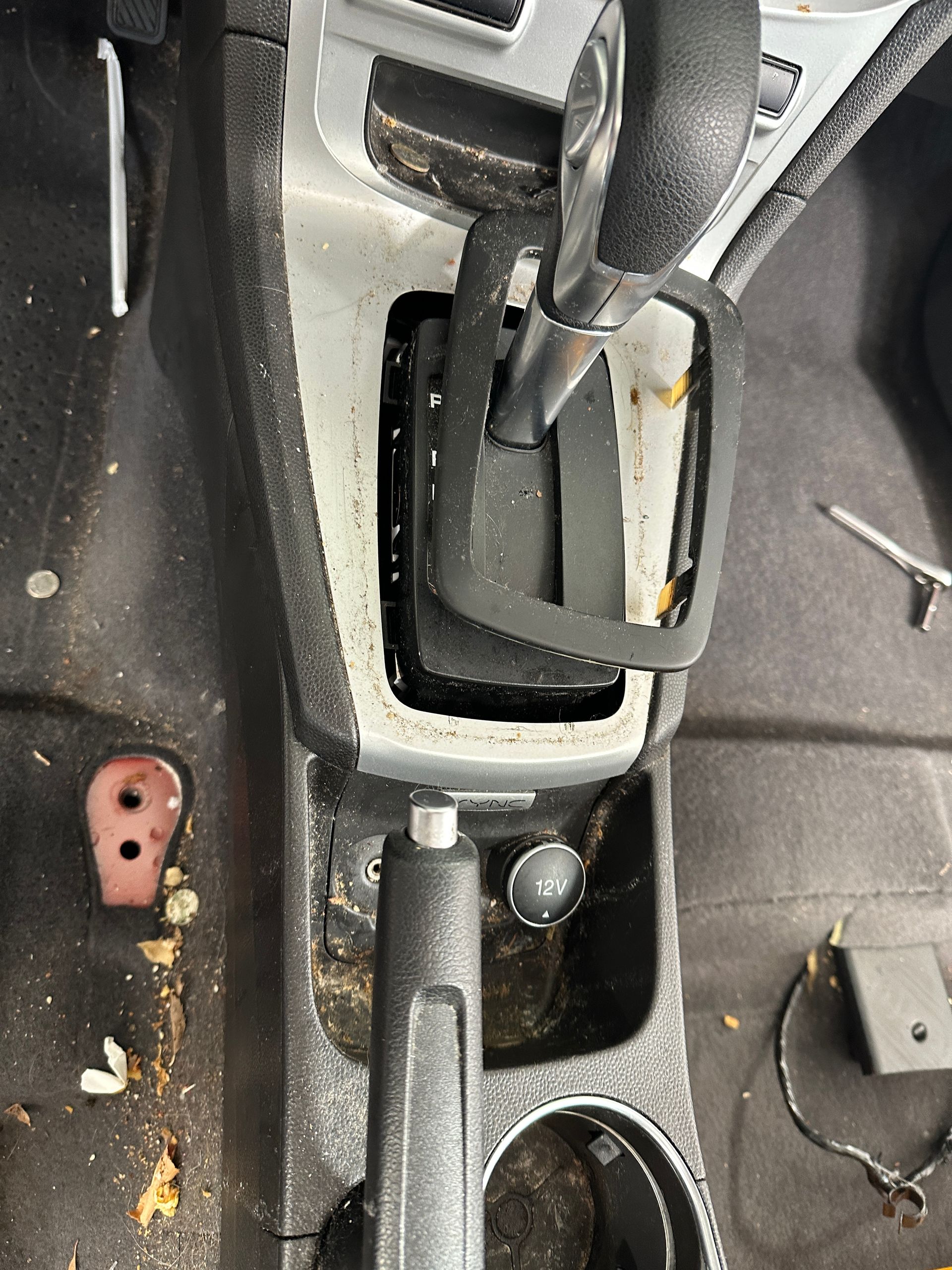 A dirty car console with a cup holder and a shifter.
