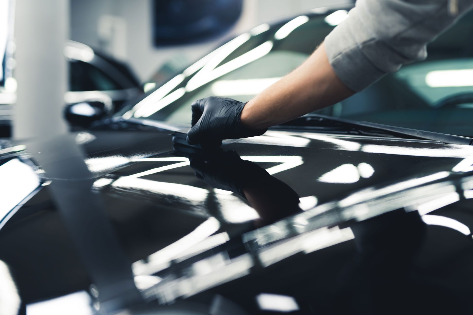 Person applying a ceramic coating to the hood of a black car with a gloved hand.