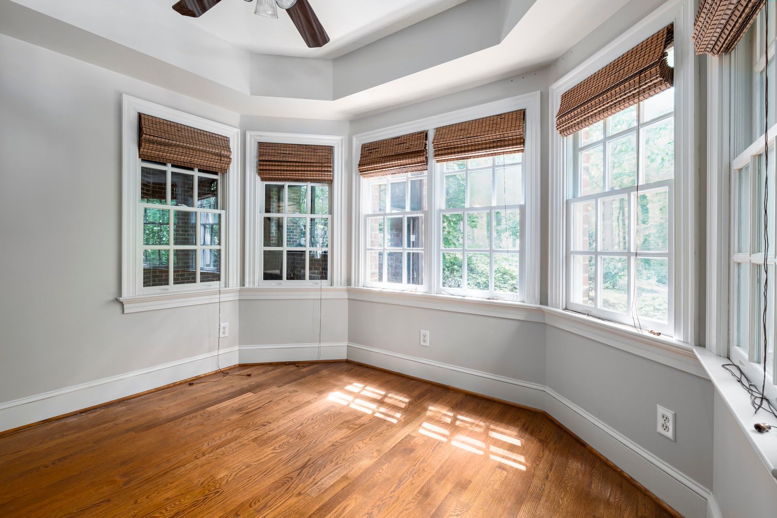 Empty sunlit room with curved bay windows, white walls, and hardwood floors