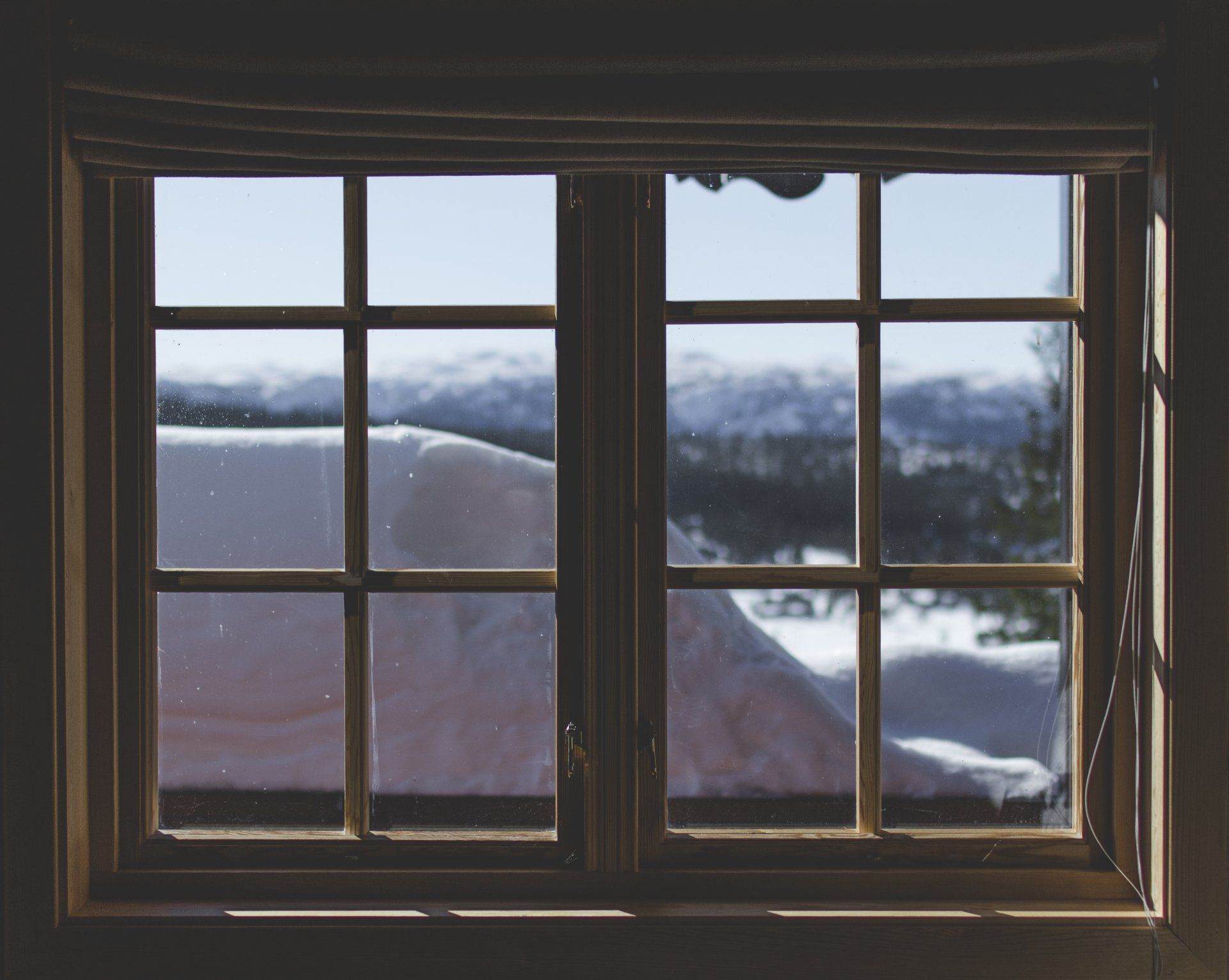Window view of snowy mountains and clouds, framed by dark wood indoors