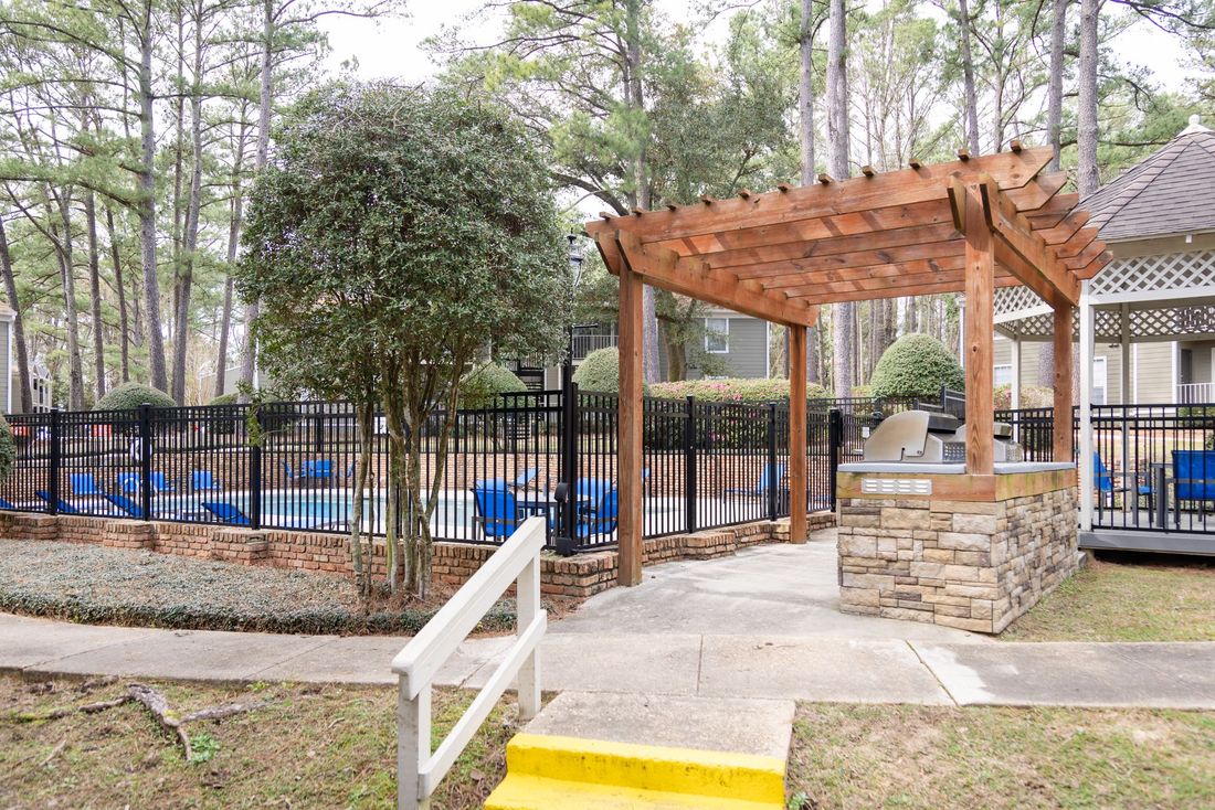 Pool area with pergola, grill, and wrought-iron fence. Blue pool chairs are visible.