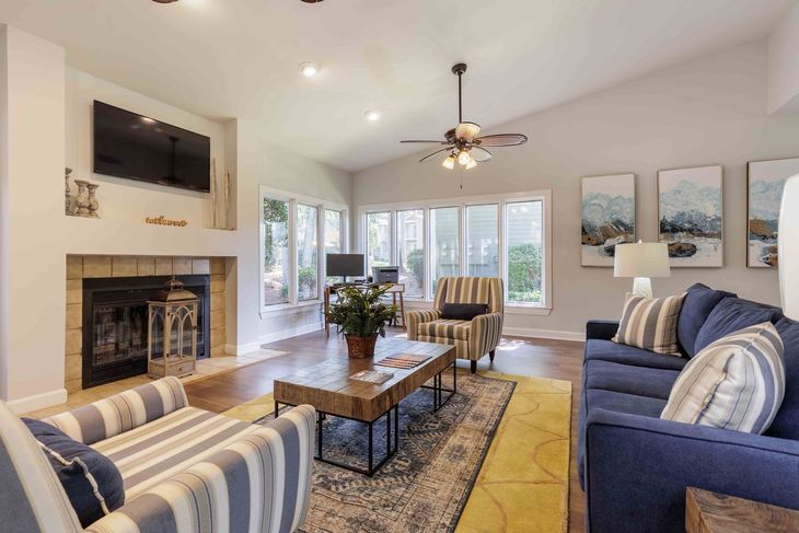 Blue and striped furniture, fireplace, TV, and three landscape paintings.