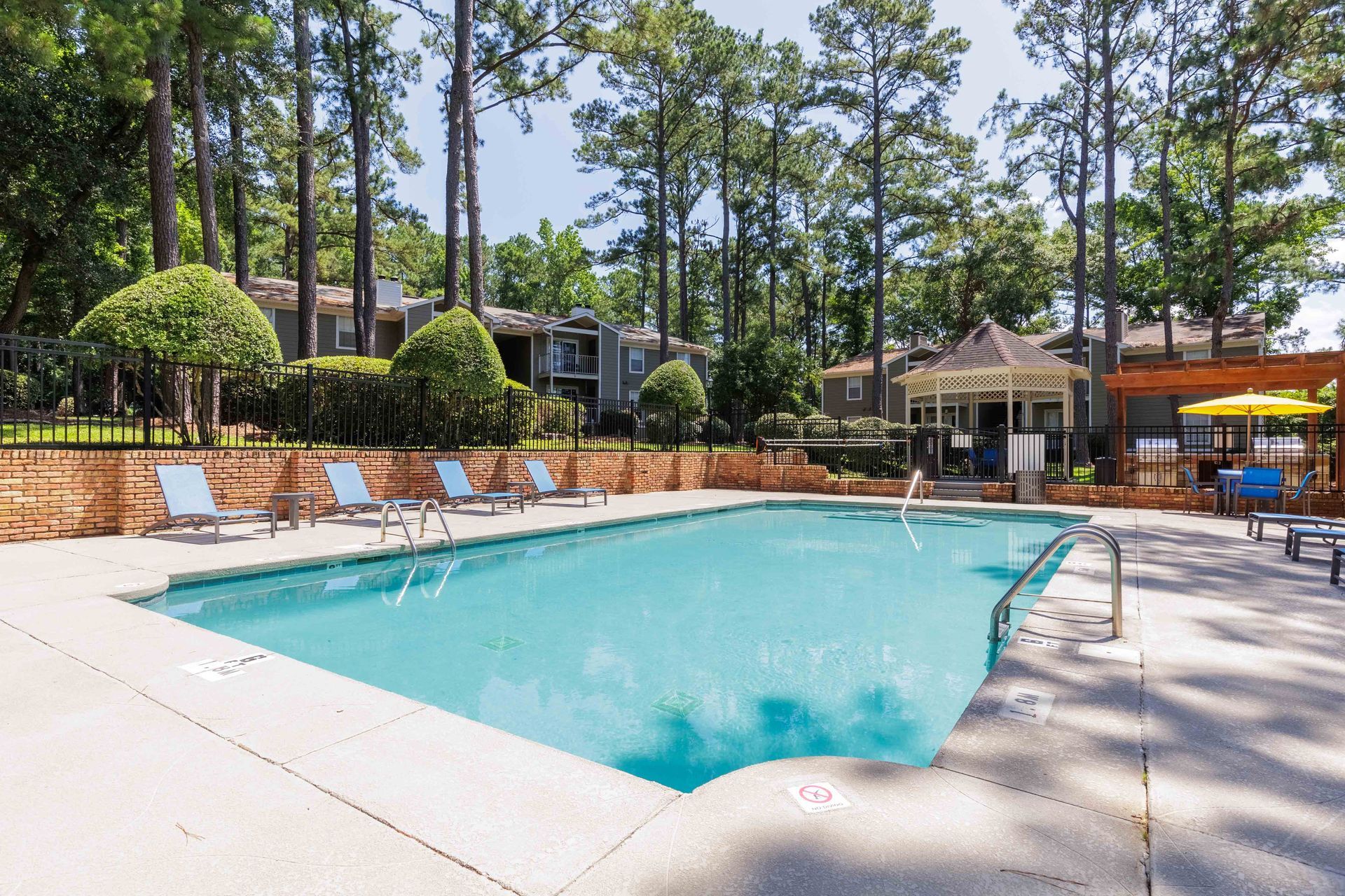 Swimming pool surrounded by lounge chairs, gazebo, and apartment buildings.