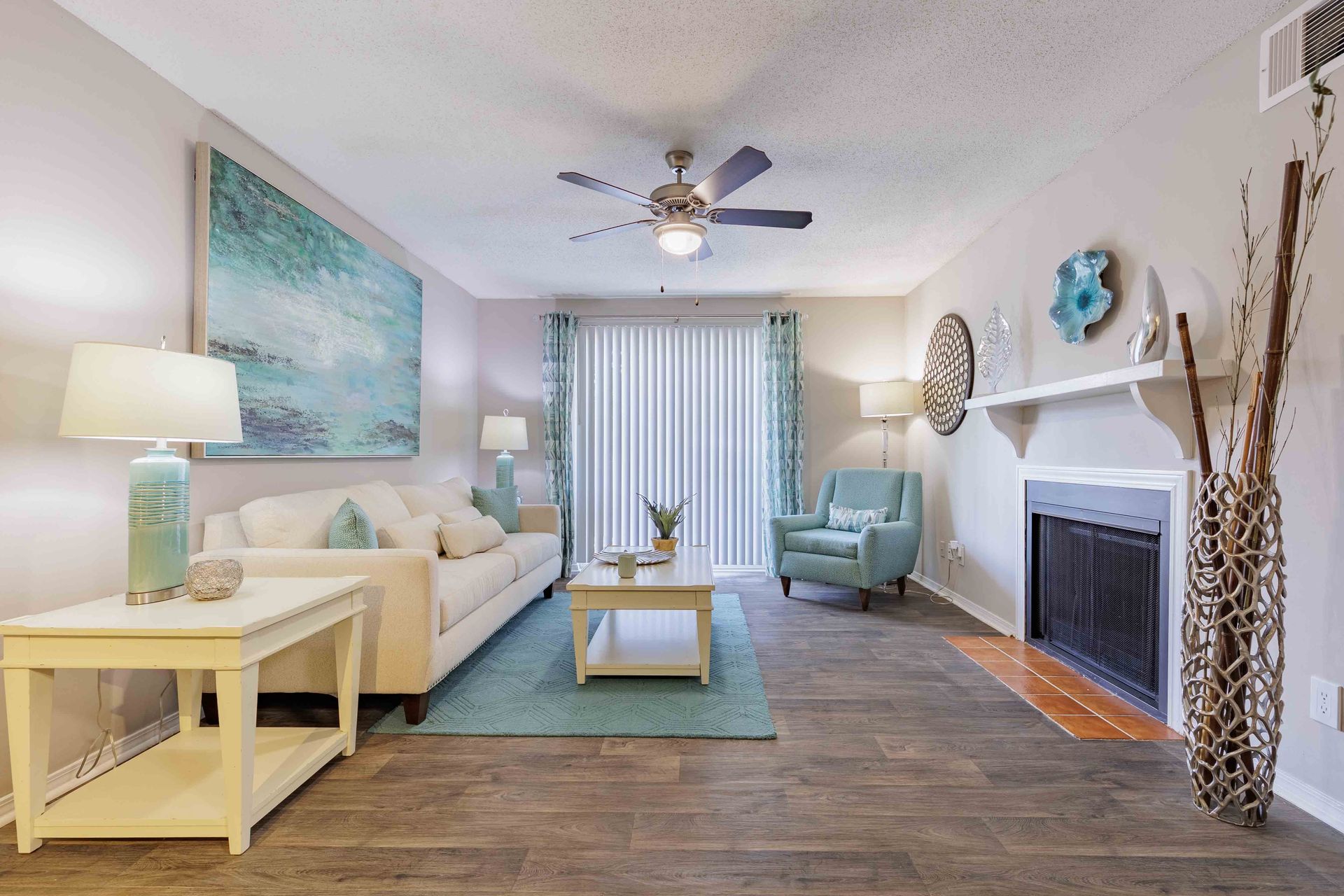 Living room with white sofa, blue accents, fireplace, wood flooring, and ceiling fan.