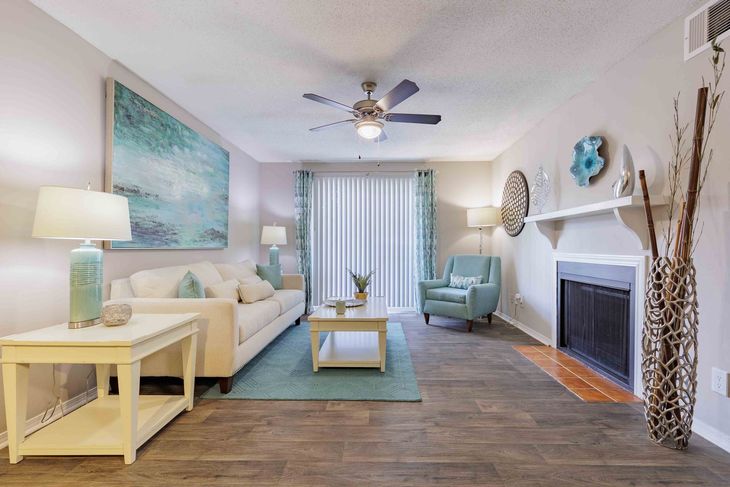 Living room with white sofa, blue accents, fireplace, wood flooring, and ceiling fan.