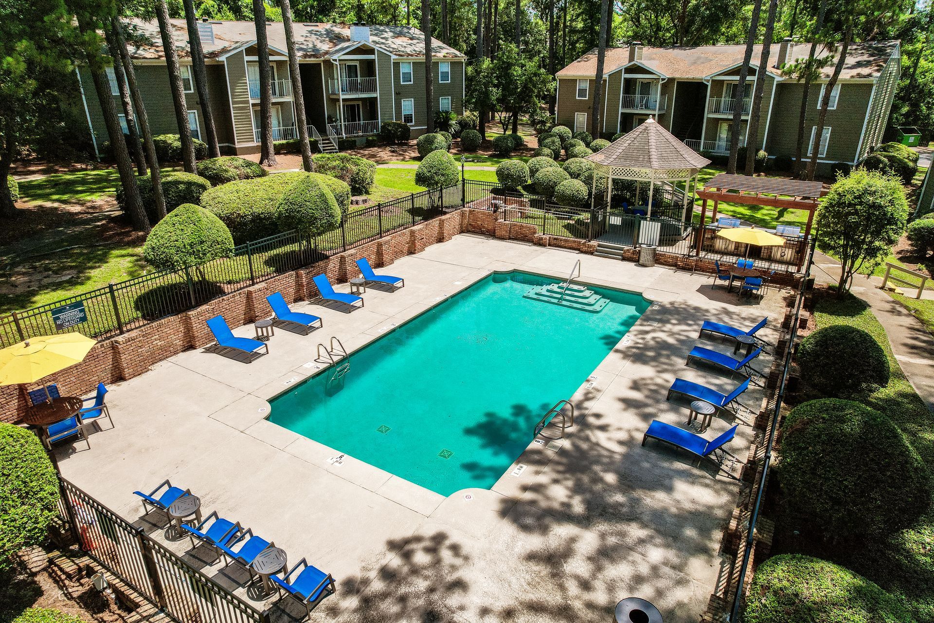Swimming pool surrounded by lounge chairs, gazebo, and apartment buildings.