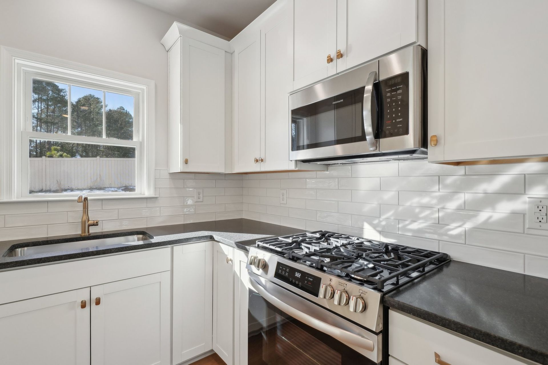 A kitchen with white cabinets , a stove , a microwave , and a sink.