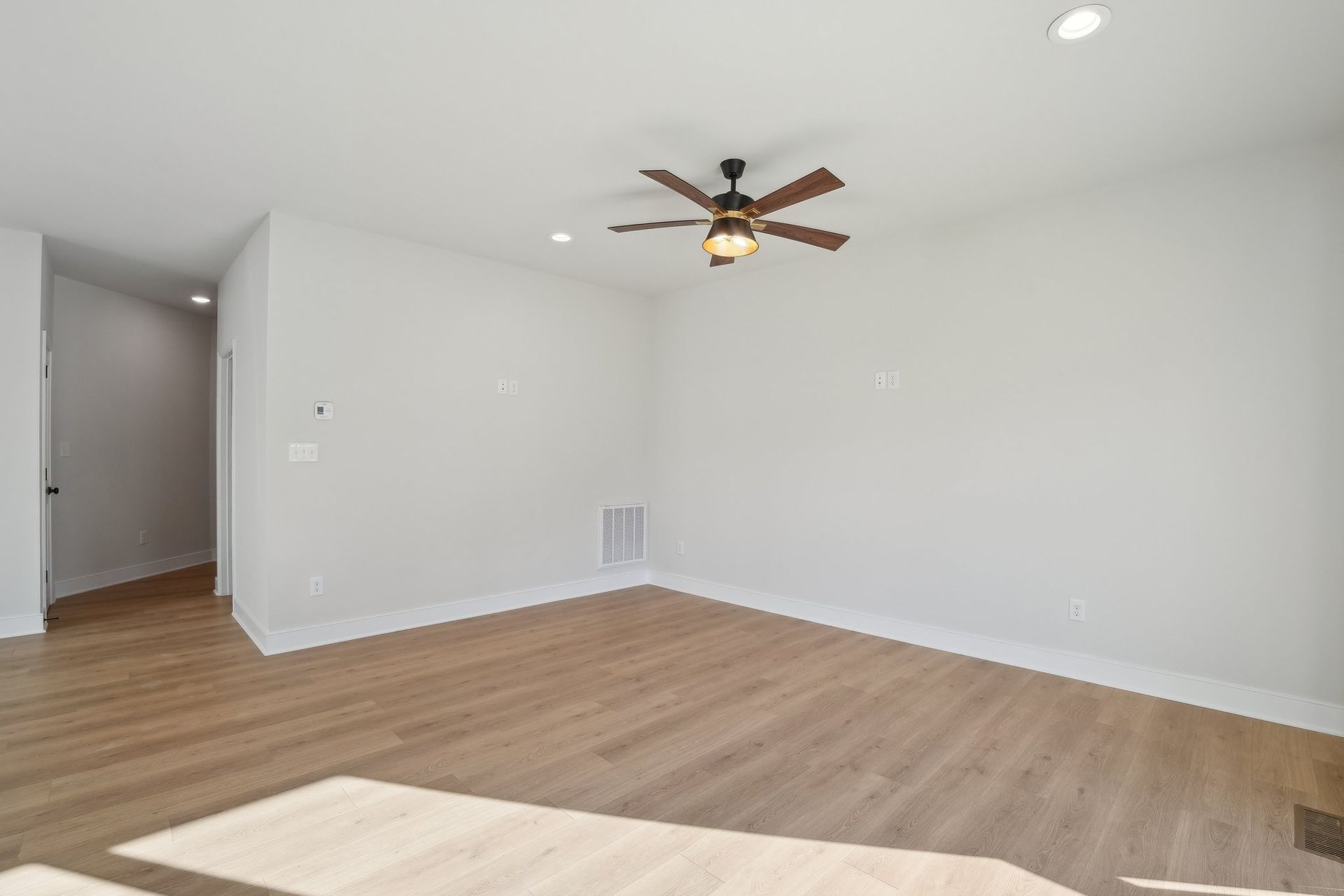 An empty living room with hardwood floors and a ceiling fan.