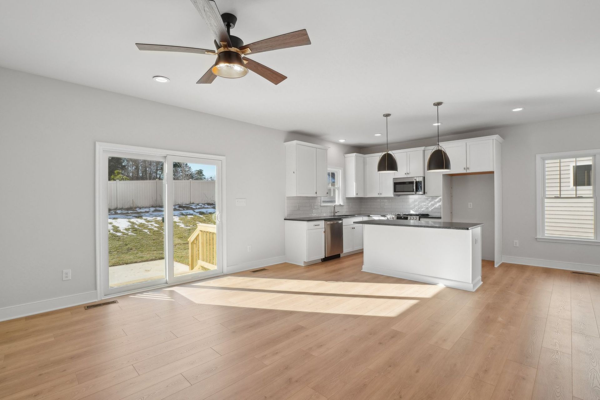An empty kitchen with a ceiling fan and sliding glass doors.