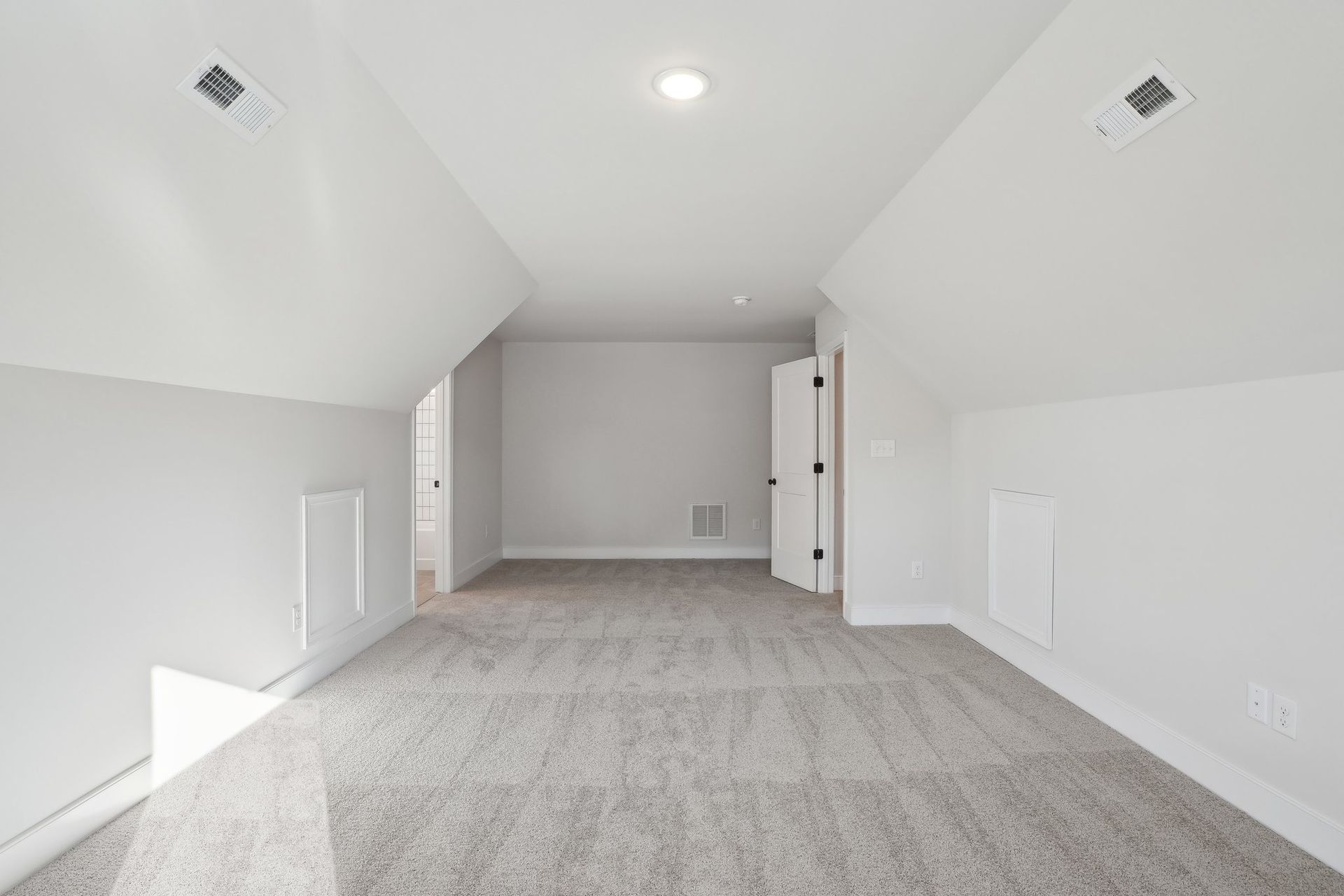An empty attic with a carpeted floor and white walls.