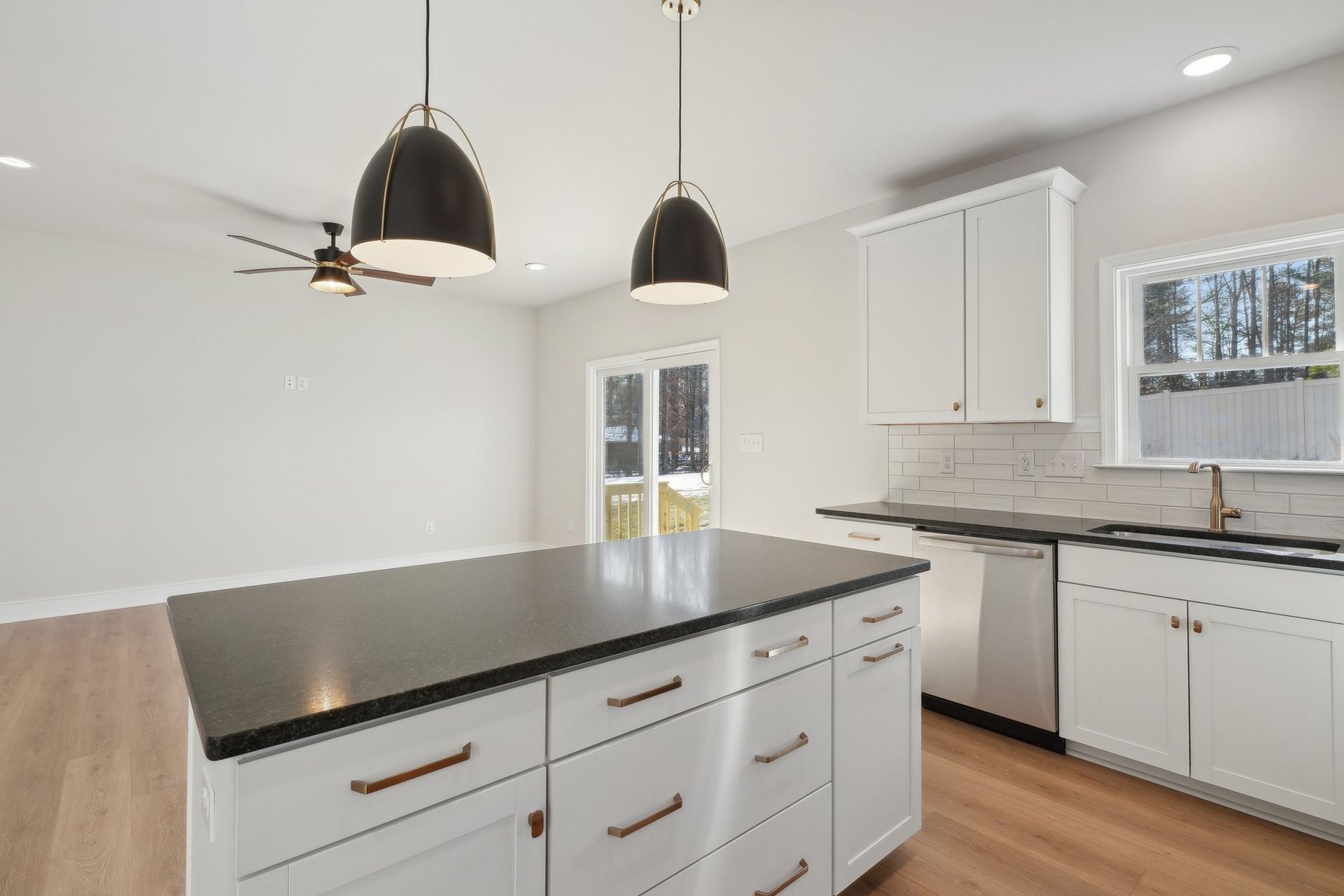 A kitchen with white cabinets , black counter tops , stainless steel appliances and a large island.