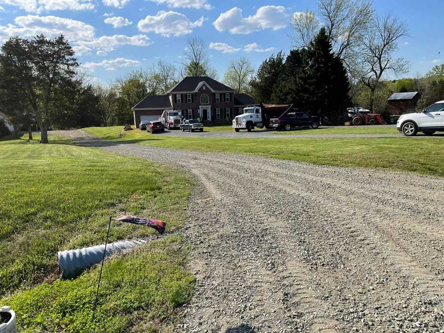 A gravel road with trees in the background and a car parked in the middle of it.