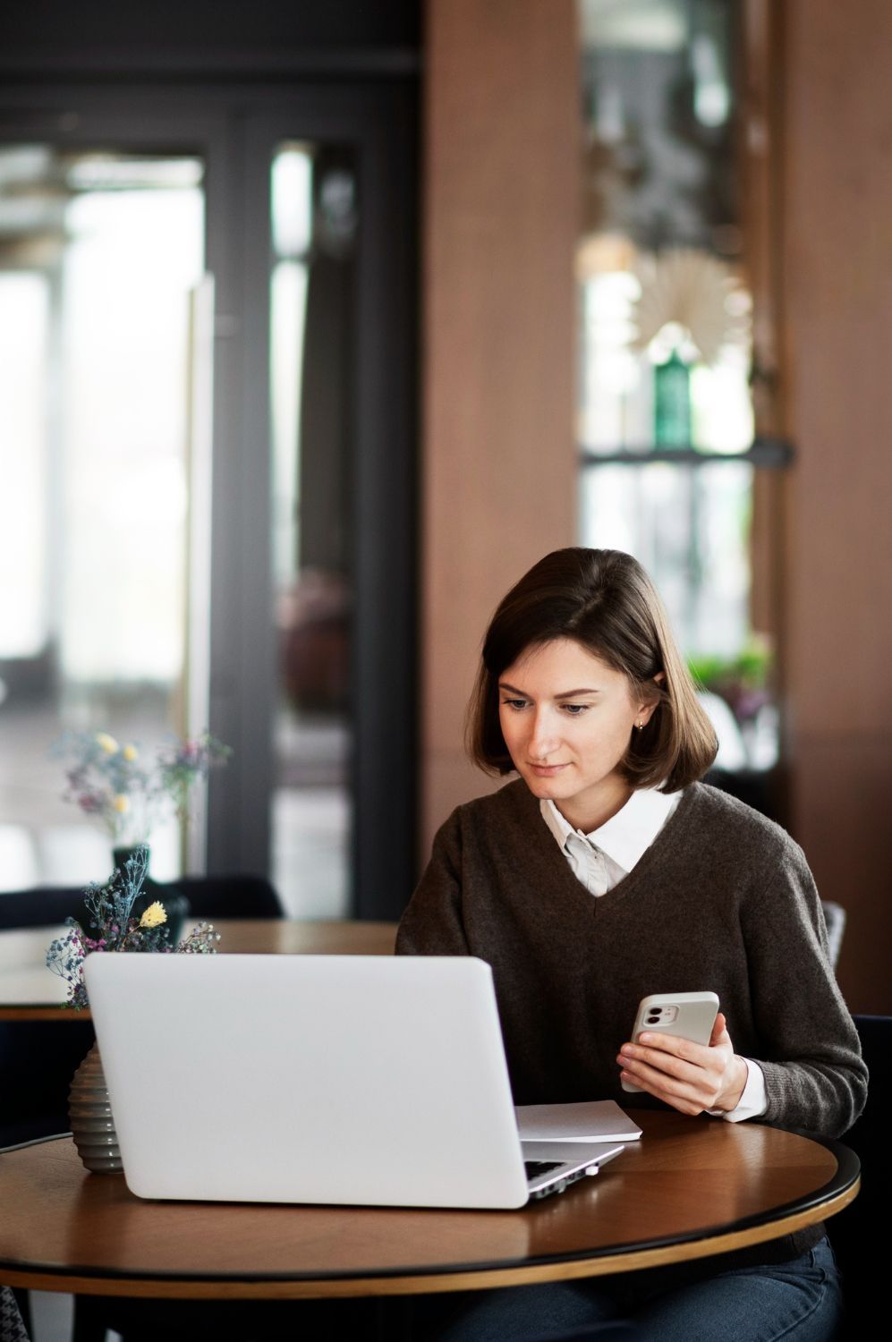 Woman sitting at a table with laptop and phone, indoors, focused.