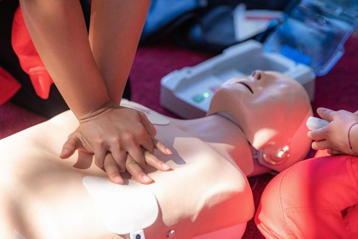 Hands performing CPR on a training dummy, with an AED nearby.