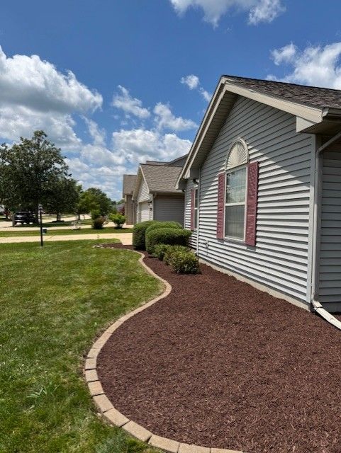 Man laying brick pathway, kneeling on ground. Other men walk in background. Outdoors.