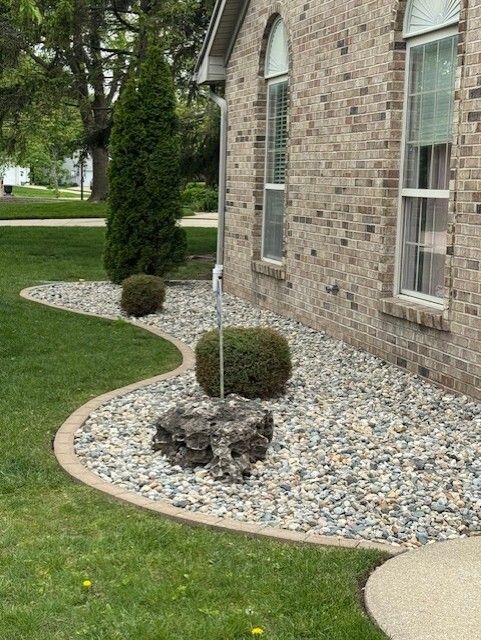 Landscaped yard with stone bed, green grass, and brick house.