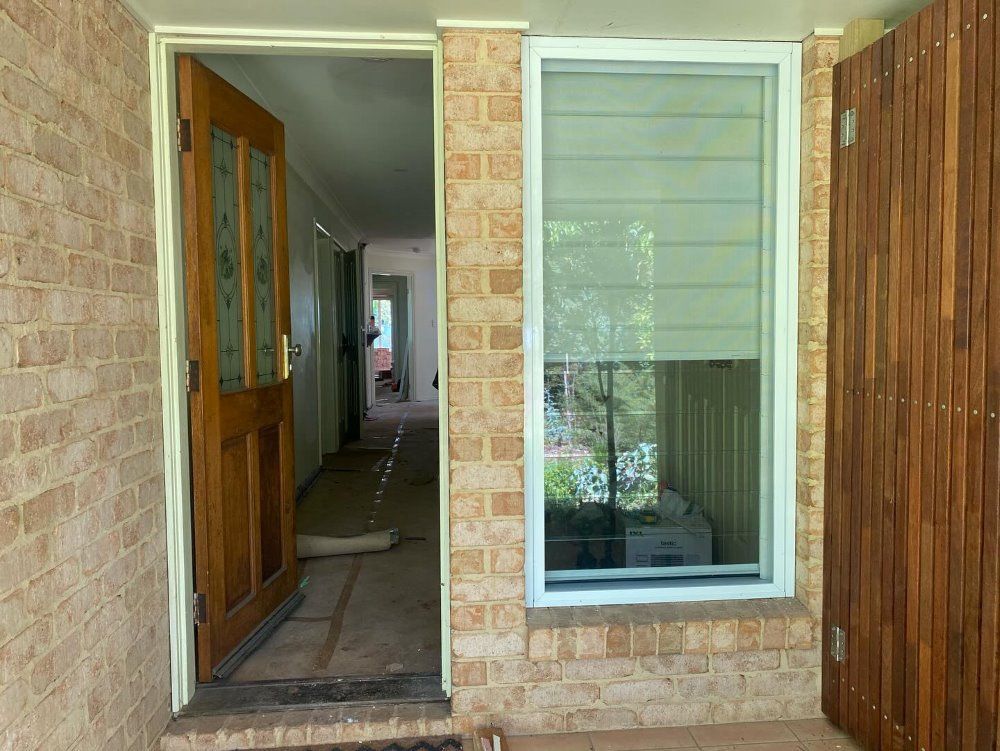 A Brick House with A Wooden Door and A Window — Boambee Gauze 'n' Glass in Harbour, NSW