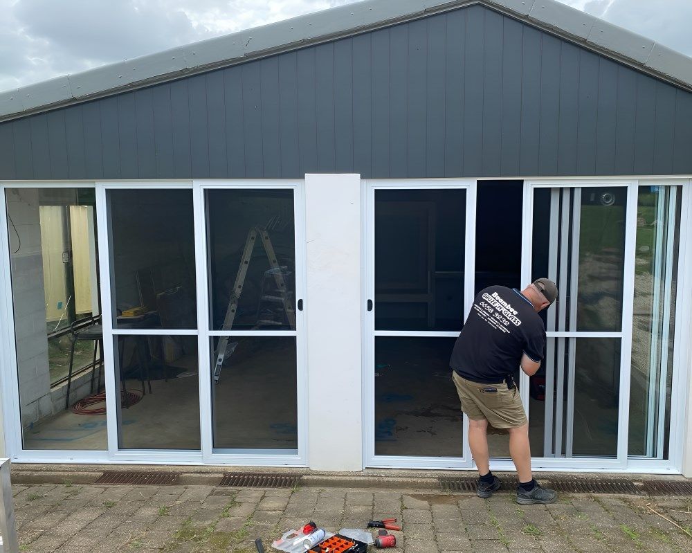 A Man Is Working on A Sliding Glass Door — Boambee Gauze 'n' Glass in Harbour, NSW