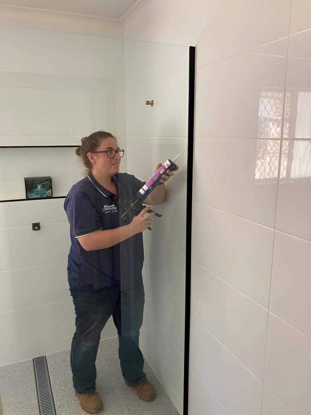 A Woman Is Installing a Shower Door in A Bathroom — Boambee Gauze 'n' Glass in Harbour, NSW