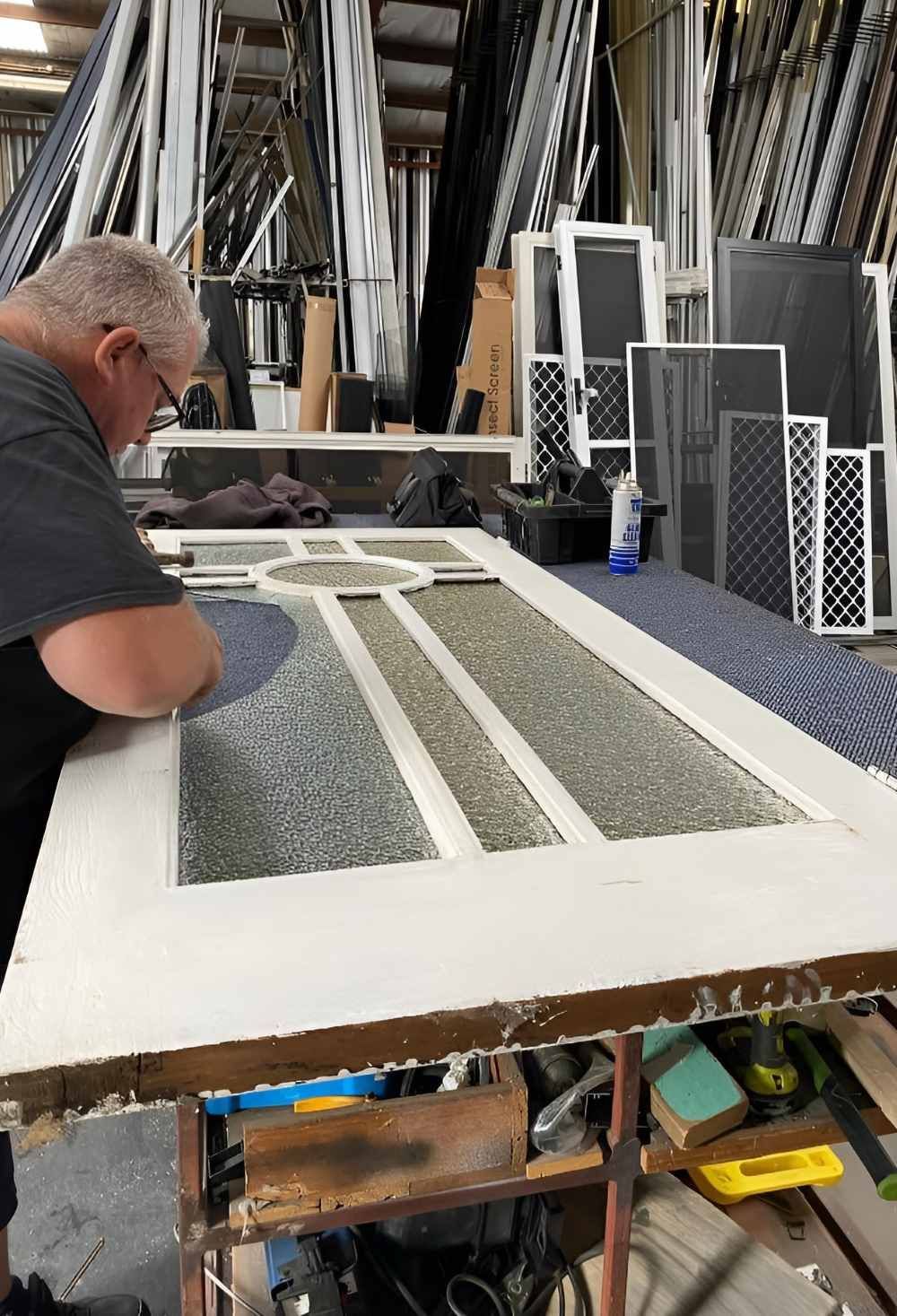 A Man Is Working on A Door in A Factory — Boambee Gauze 'n' Glass in Harbour, NSW