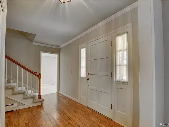 Entryway with hardwood floors, white doors, and staircase with wood railing.