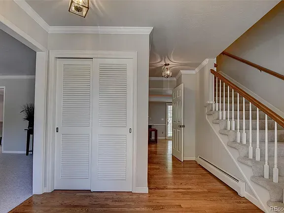 Entryway with wooden floors, white walls, closet doors, and staircase.