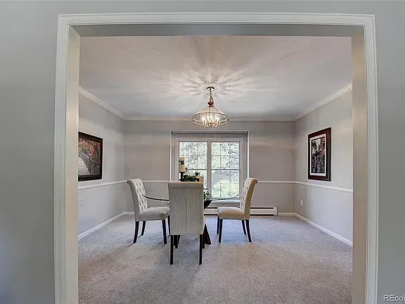 Dining room with table, chairs, window, and chandelier. Light gray walls with white trim and a gray carpet.