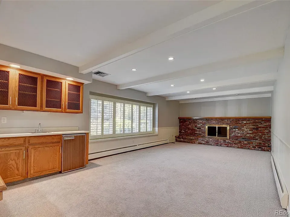 Empty basement room with a fireplace, built-in bar, and carpet. Beige and brown tones.