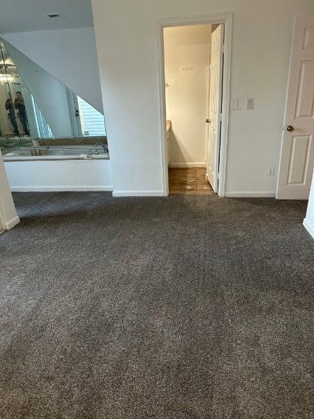 A room with gray carpet, a bathroom door open, and a sunken bathtub.