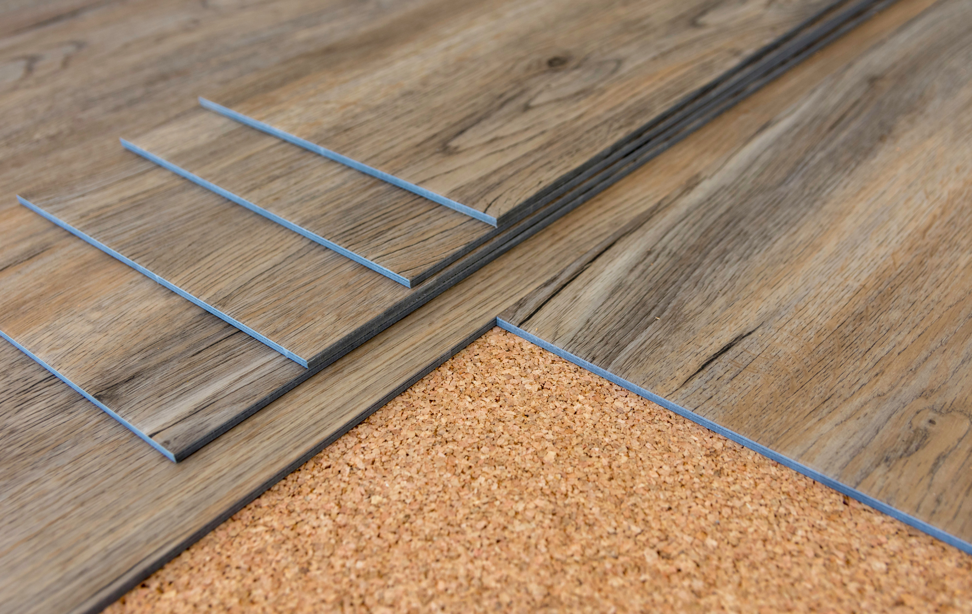Wood-look laminate flooring planks being installed over a cork underlayment; close-up.
