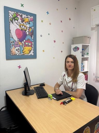 Médica sentada en su escritorio, con estetoscopio visible. 