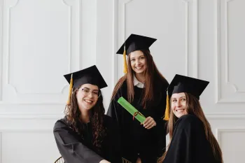 Three graduates in black caps and gowns smiling, one holding a diploma.