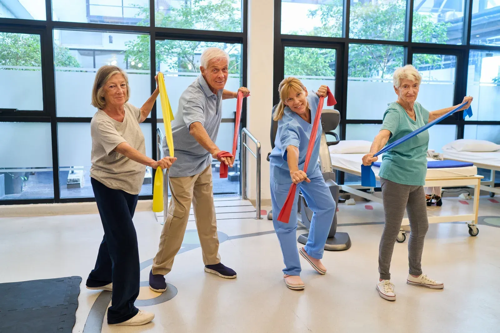 Four people using resistance bands for exercise in a therapy room.