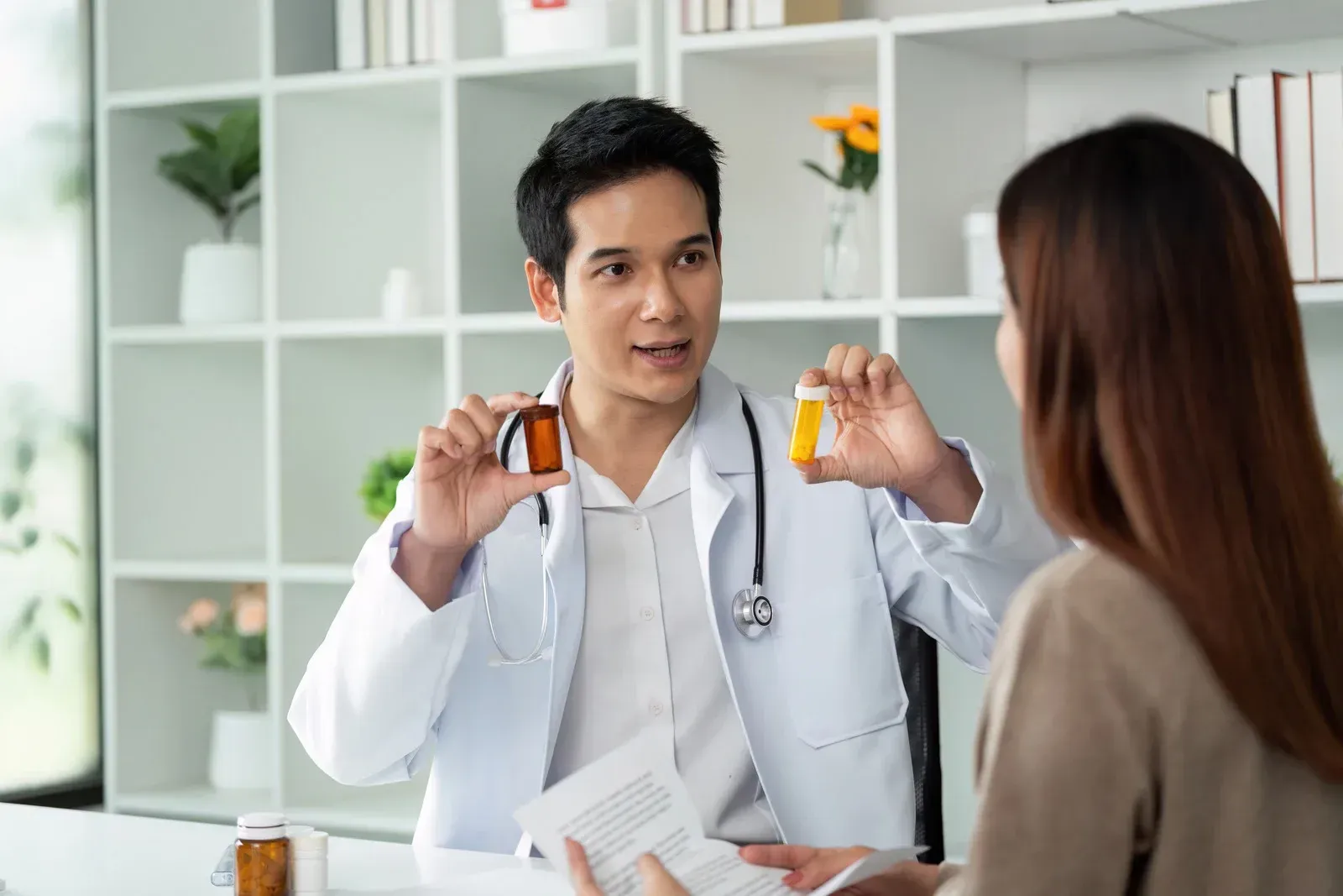 Doctor holding pill bottles, explaining medication to a patient in a medical office.
