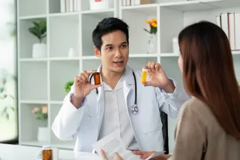 Doctor holding pill bottles, explaining medication to a patient in a medical office.