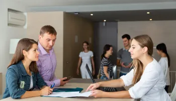 People reviewing documents at a table; others in background; office setting.