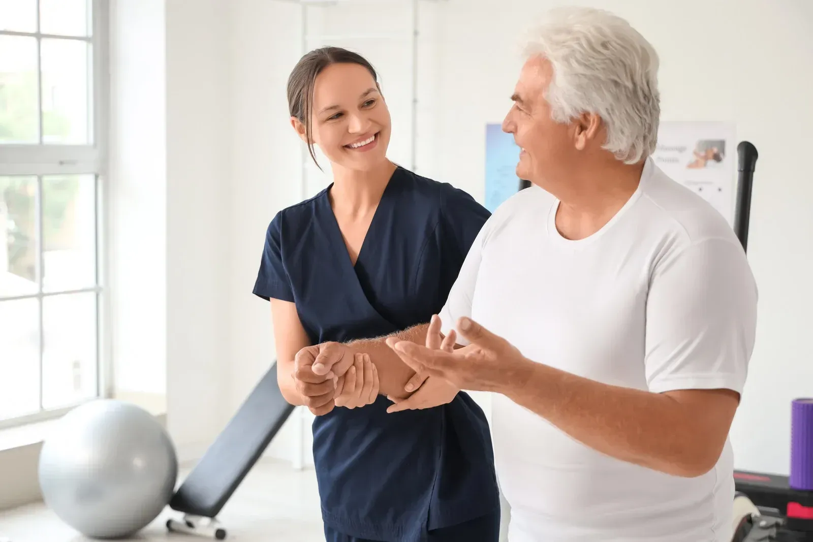Therapist assisting a patient in walking. They are in a clinic, smiling.